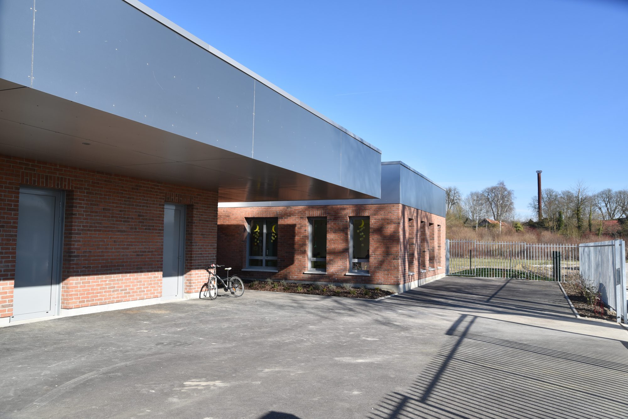 Accueil périscolaire de Namps-Maisnil vu depuis la cour : assise en brique rouge et couronnement métallique clair