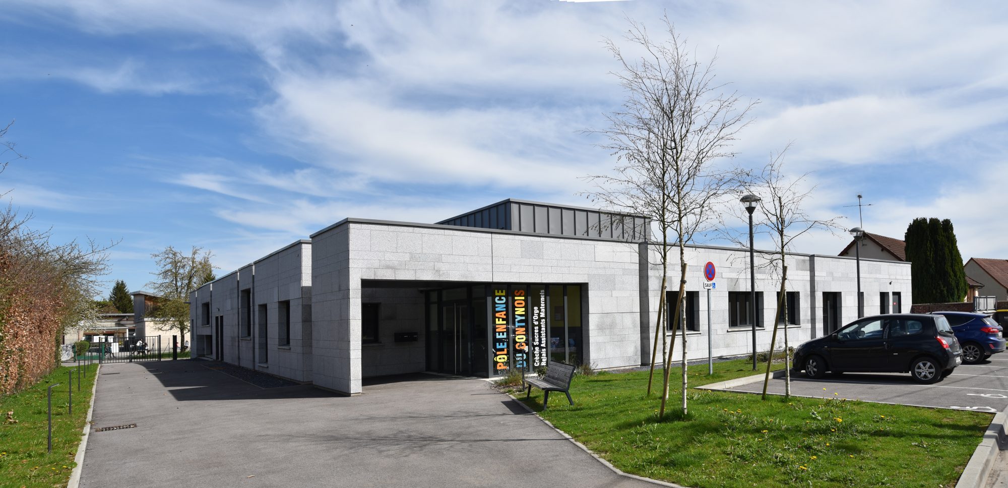 Crèche et RAM de Conty vus depuis la rue : bâtiment bas en béton clair, parvis dégagé et volume émergent en toiture