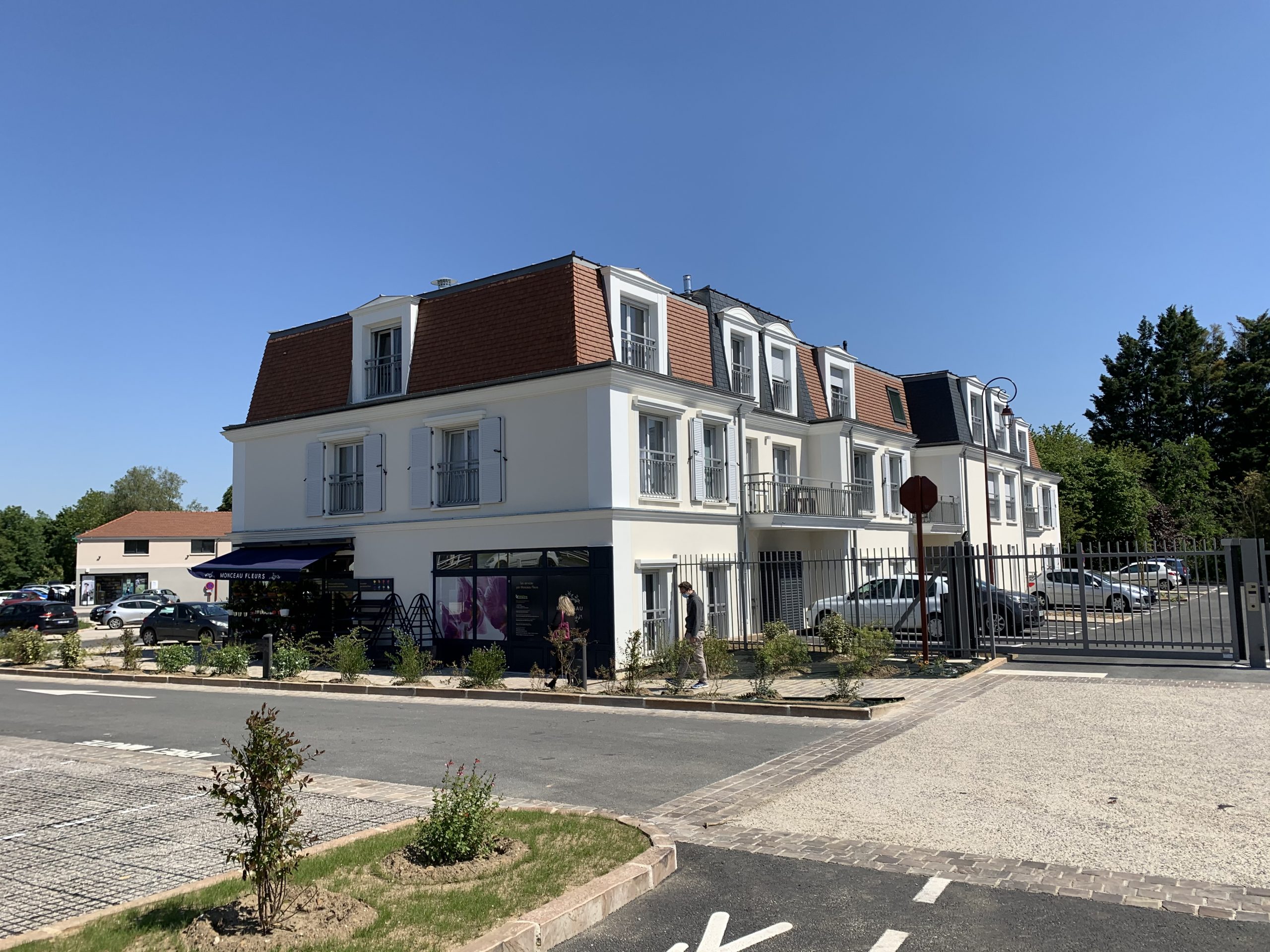 Résidence l'Allée du Château à Chaumontel : enduit clair, toiture à brisis et commerce en rez-de-chaussée