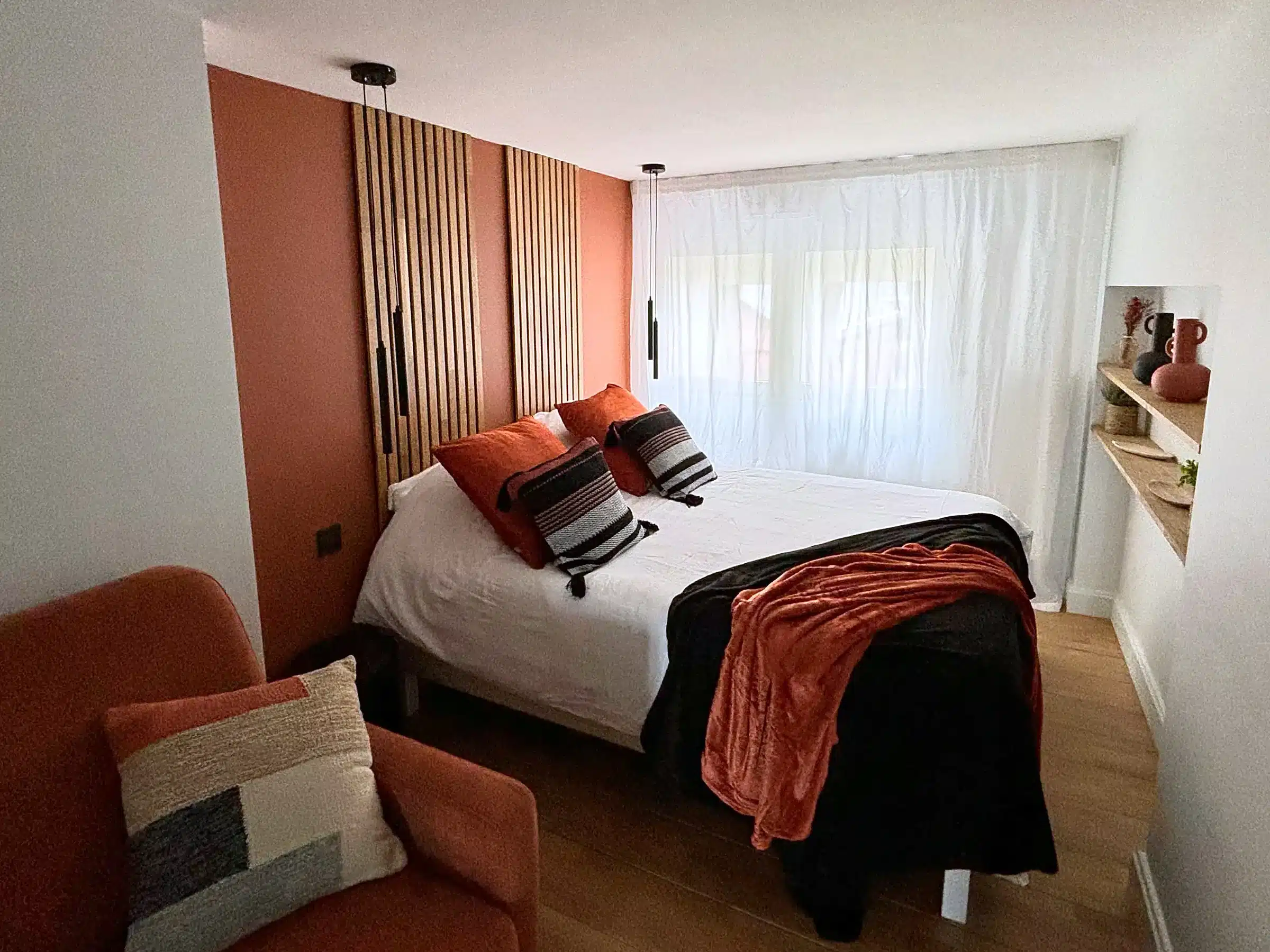 Chambre aux tasseaux de bois sur fond terracotta, voilages devant la fenêtre