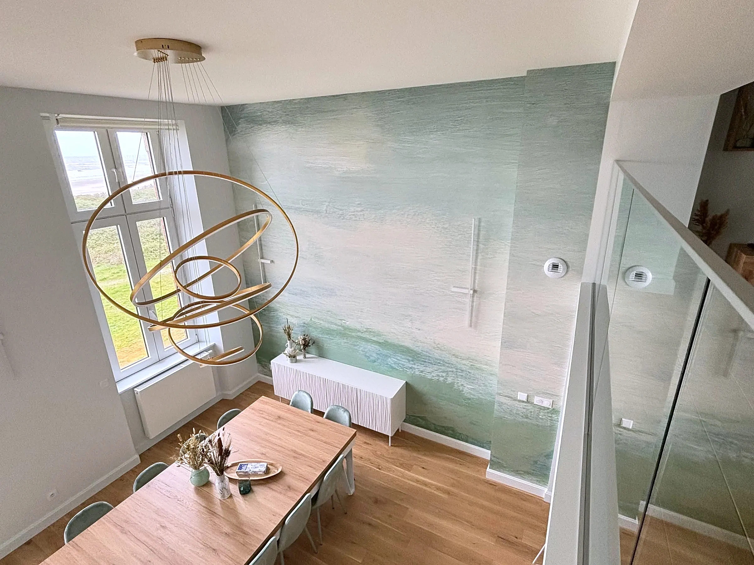Vue depuis la mezzanine en hêtre massif sur le séjour, sa fresque murale et la fenêtre ouverte sur la dune