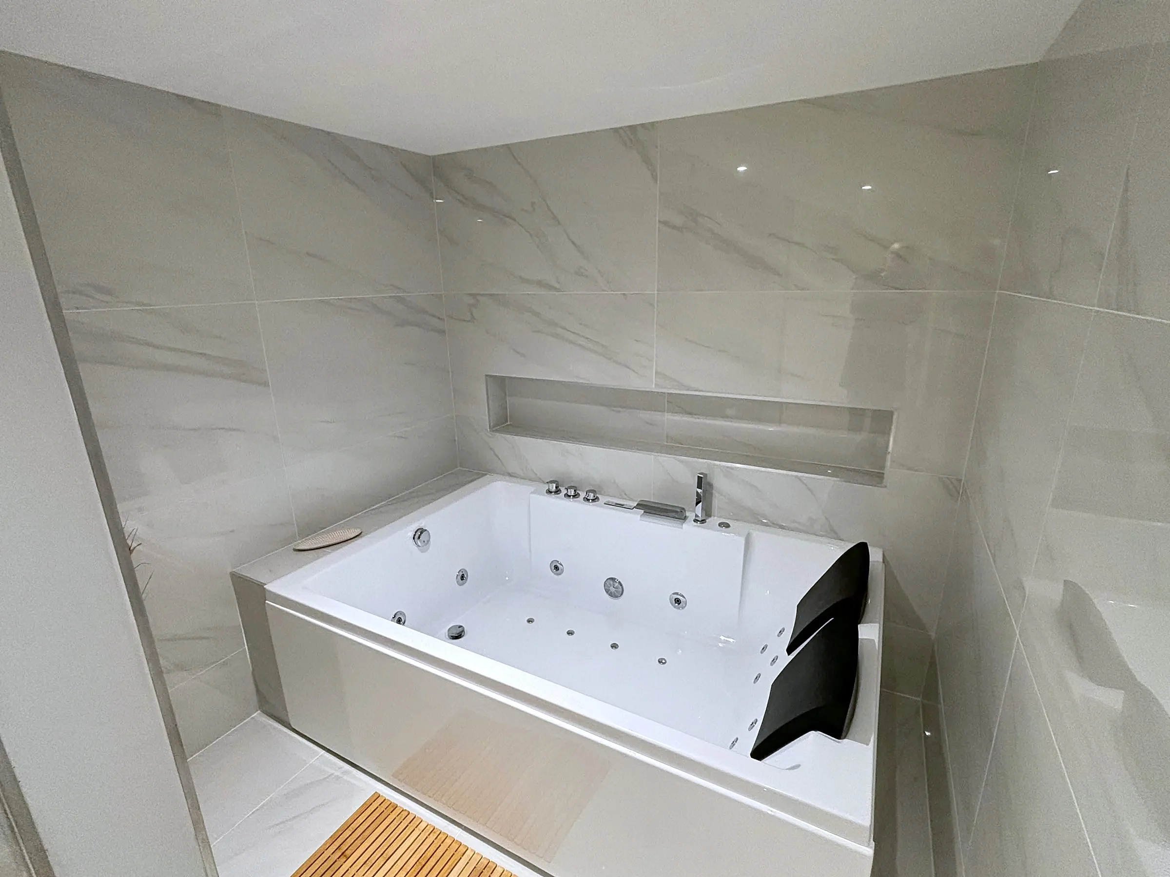 Salle de bains en grès grand format effet marbre avec baignoire balnéo et niche maçonnée