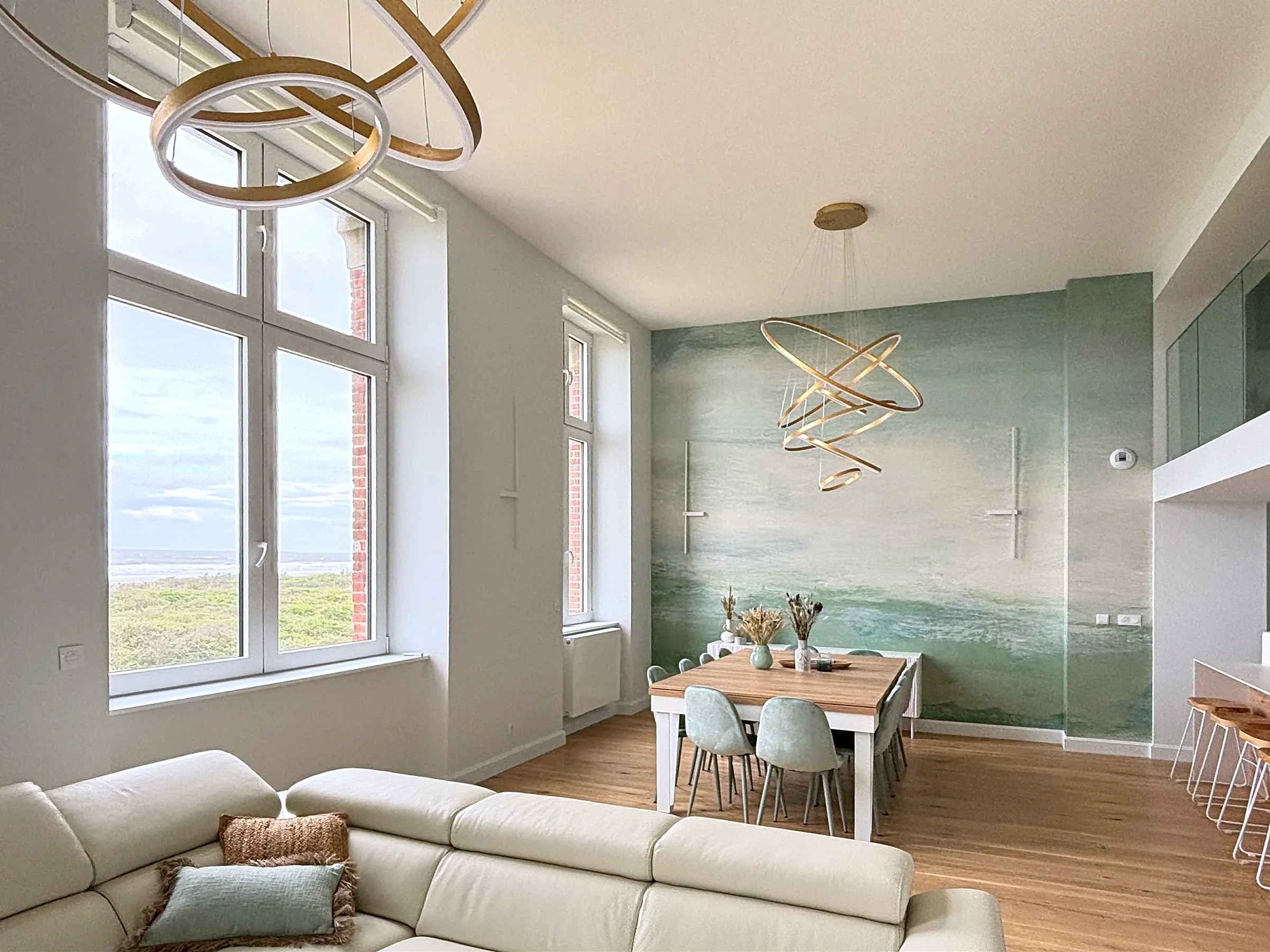 Salon et salle à manger en double hauteur devant une fresque murale aux tons d'eau, appartement vue mer à Berck-sur-Mer